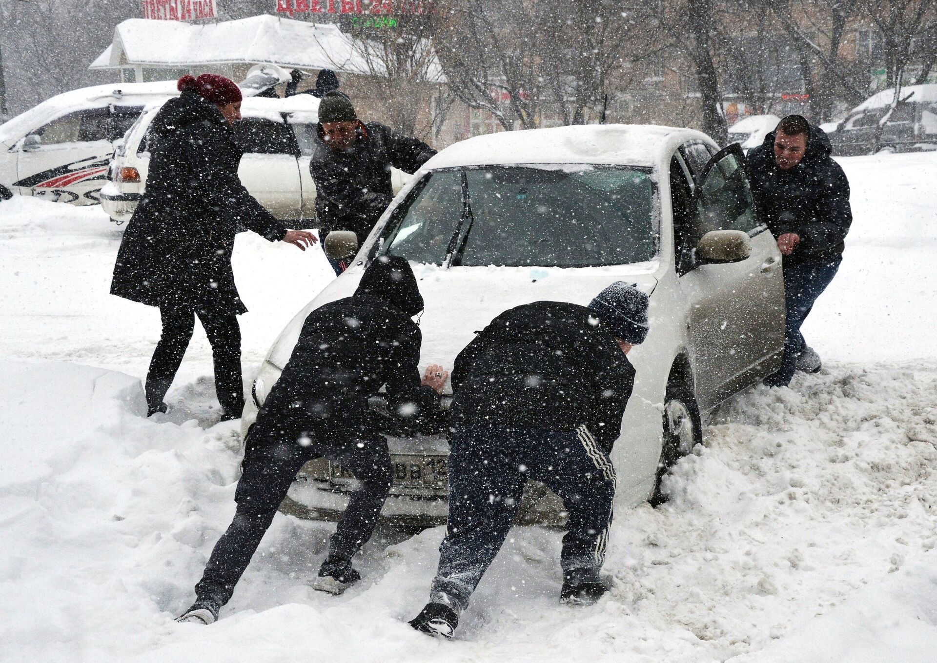 Село качки занесенное снегом. Выталкивать из сугроба машину. Толкают машину. Толкают машину зимой. Толкать машину из снега.