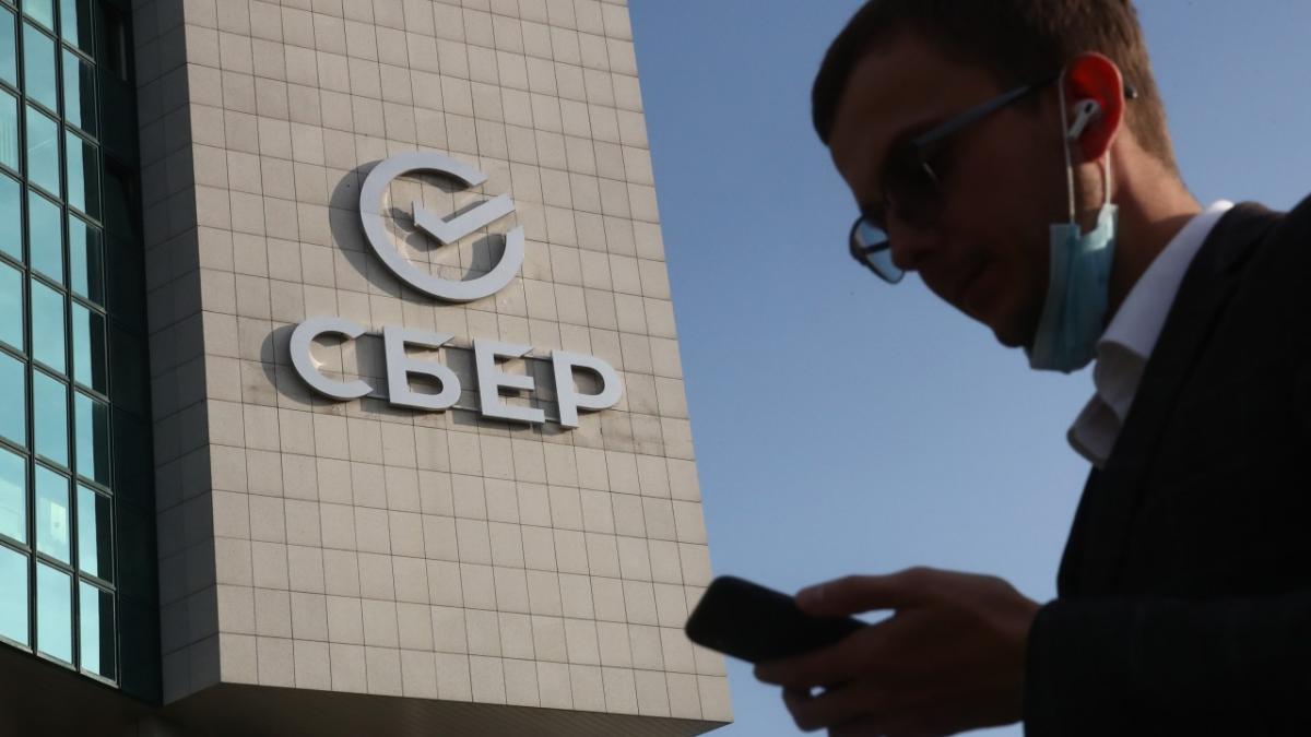 Мужчина с телефоном стоит у здания Сбербанка сбербанк криптовалюта